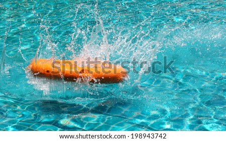 Orange life buoy is splashing with clear blue water in swimming pool, for the emergency case