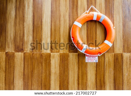 The orange life buoy with the wood wall background, near the swimming pool, for safety and rescue