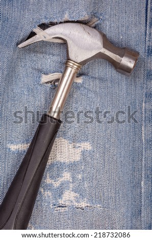 Hammer black handle tool with torn blue jeans pattern background, concept for fixing and useful maintenance.