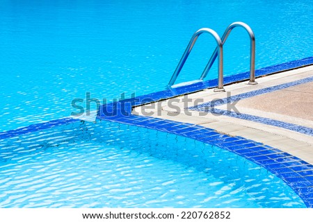 A view of curved light clear blue swimming pool with steel ladder, outdoor swimming pool.