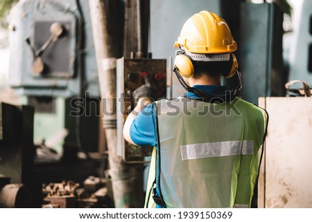 Back view of Work at factory.Asian worker man  working in safety work wear with yellow helmet l ear muff.machanic male asia in factory workshop industry machine professional