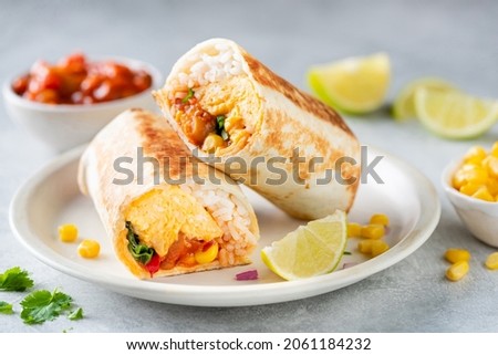 Breakfast vegetarian burrito wrap with omelette and vegetables on a plate. Tortilla wrap sandwich