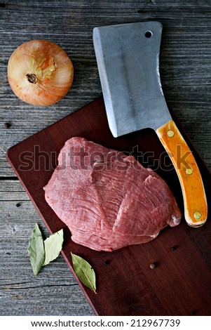 Meat steak on wooden table with butcher knife, onion and bay leaves. Still life