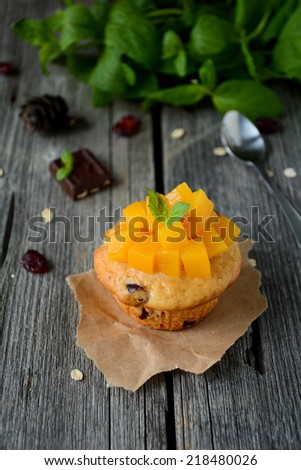 Cupcake with cranberries topped with chopped peaches and mint leaf on wooden table top, vertical image