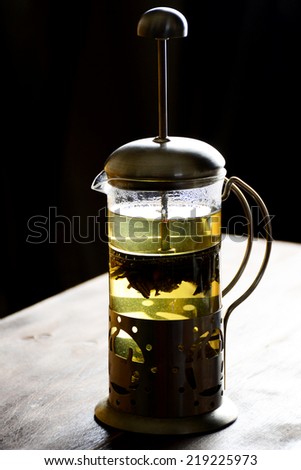 French press with green tea on wooden table, black background. Atmospheric low key image