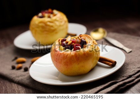 Two stuffed baked apples with oats, cranberries, raisins, almonds and honey on white dessert plates, Christmas sweet