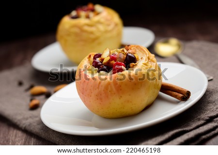 Two stuffed baked apples with oats, cranberries, raisins, almonds and honey on white dessert plates, Christmas sweet