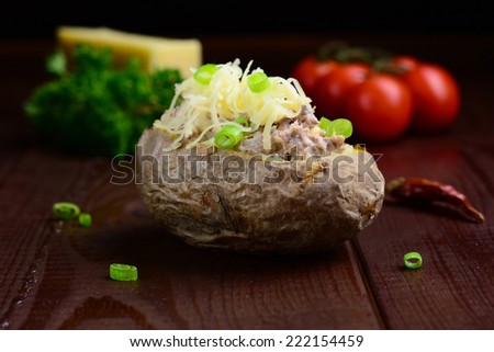 Twice baked potato stuffed with tuna and cheese garnished with green onion on dark brown wooden table. Low key photography