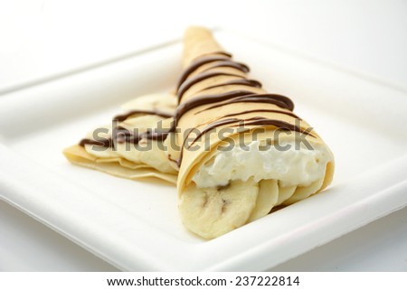 Crepe filled with whipped cream and banana slices decorated with nutella on square plate, isolated