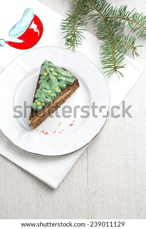 Chocolate cake with chocolate butter cream filling and dark chocolate glaze decorated with green frosting and confetti for Christmas on white plate (Prague chocolate cake). Above with copy space