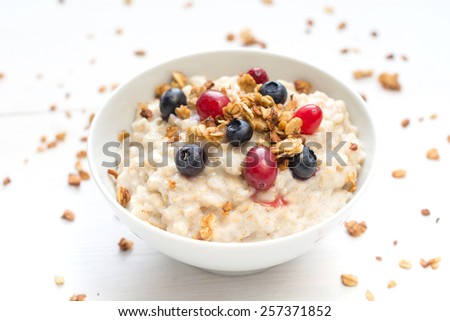 Oatmeal porridge in bowl topped with fresh blueberries, cranberries and homemade crunchy granola