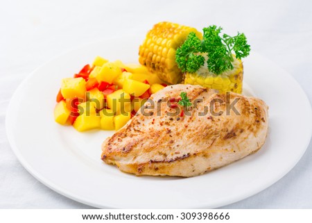Gourmet meal: grilled chicken breast with mango salsa and grilled corn on white plate, studio isolated