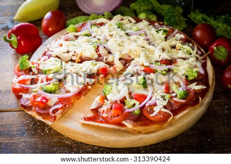 Thin crust pizza with sausages, pepper, tomatoes, broccoli and cheese on round wooden board