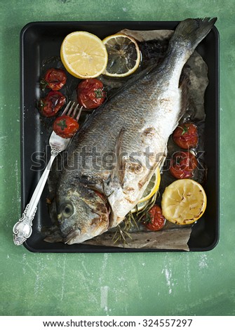 Top view of sea fish dorada grilled with rosemary, lemon and tomatoes. Prepared to eat and served in rustic style.