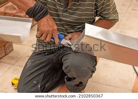 Hands of skilled workers secure the rim of the rain gutter with pliers. Stock fotó © 