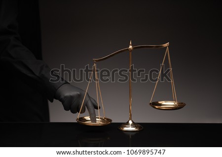Someone wearing black shirt pressing the imbalance scale on black glass desktop and black background, cheating  in a lawyer's office, Concept of injustice, espionage, partiality, law. Foto stock © 