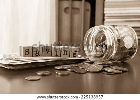 Saving word on rubber stamps place on banknotes with coins spilling out of money jars, sepia toned