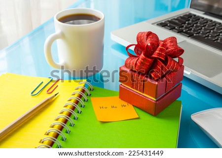 Red present box and paper note with Merry christmas message: Ho Ho Ho! place on office table with laptop, colorful diary and a cup of coffee, concept to christmas gift and holiday season