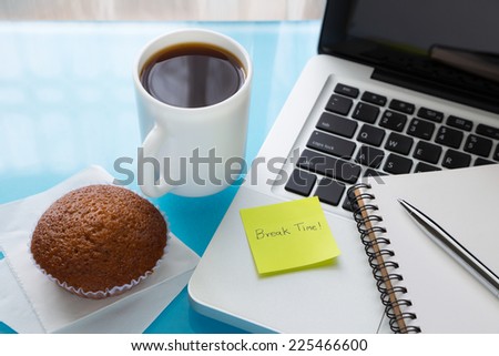 Coffee break, cupcake  and notebook place on laptop with sticky note message : Break Time, A break at work concept