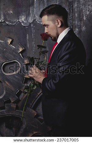 a man in a business suit on a background of the dark wall with the mechanism and with a rose in hand