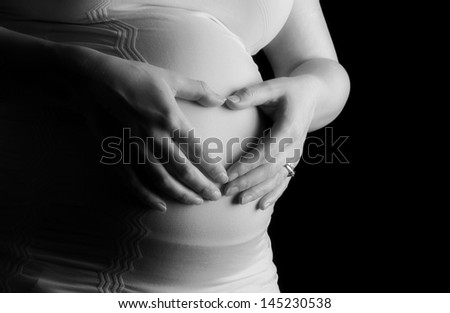 A pregnant woman with wedding ring making a heart on her belly