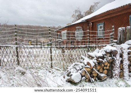 Polenitsa firewood in the courtyard of the village houses covered with snow. On the metal wires of the fence are visible ice icicles.