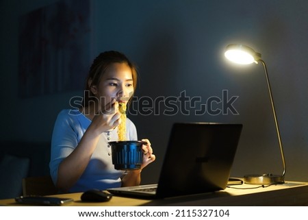Asian freelancer smart business woman eating instant noodles while working on a laptop in the living room at home at night happy Asian girl sitting on a desk overtime enjoying relaxing time Сток-фото © 