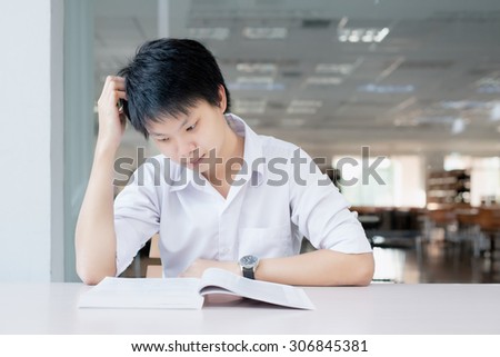 Sad Asian student in uniform reading book in classroom