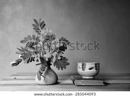 still life with vase,tea cup and old book on wooden table.black and white filter effect.