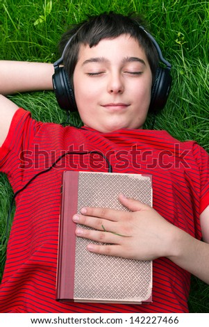 Boy is lying on a grass and he is listening audio book