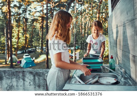 Similar – Foto Bild Teenager-Mädchen spült während der Ferien auf dem Campingplatz mit Hilfe ihrer jüngeren Schwester in der Außenküche Töpfe und Teller ab