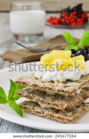 rye bread with cottage cheese, mango and berries of mountain ash in the plate on white wooden background. health and diet food. selective focus