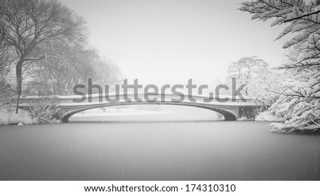 Bow Bridge and the Lake being covered in snow in winter. Black & White photography of Central Park\'s Bow Bridge and the Lake in winter during a snowfall. Wintertime in NYC.