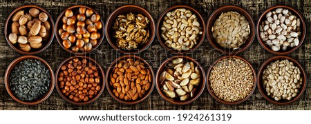 Peanuts, cashews, hazelnuts, almonds, walnuts, pecans, Brazil nuts, sunflower seeds, pumpkin seeds, pistachios close up. Nuts in clay bowls on a brown wooden board. Nuts on a shabby table.