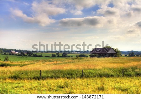 an old hay barn on an open plot of land with wild grass in the foreground.