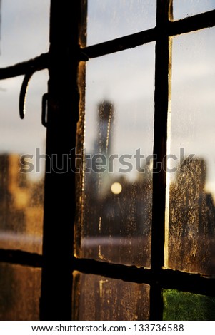 A window stained with drop marks enhanced by the sun\'s backlight, and blurry Lower Manhattan skyline in the background behind the glass.