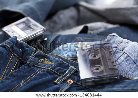 A couple of blank audio cassettes, one of them still in its box, laid on the background of various pairs of jeans pants.