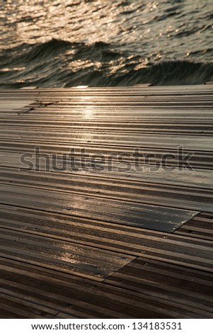 A wooden deck completely soaked wet by the waves of the gushing sea hitting against it on a winter day.
