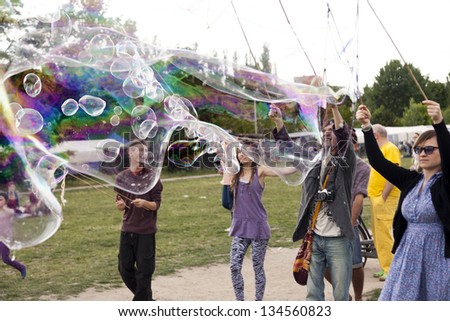BERLIN - JUNE 10: A group of young adults making giant soap bubbles on an early summer day at Mauerpark, with the flea market in the background on June 10 2012 in Berlin, Germany.