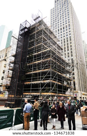 NEW YORK - NOV 20: Pedestrians walking by the traditional Rockefeller Center Christmas tree that\'s being prepared for the famous Christmas ceremony on November 20 2012 in New York, New York.