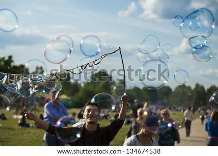 BERLIN - JUNE 10: A young man making giant soap bubbles on a Sunday afternoon at Mauerpark, with a crowd all around. On June 10 2012 in Berlin, Germany.