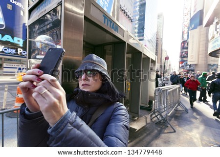 NEW YORK - NOV 6: Unidentified woman in her 30\'s using her smartphone to take photos in times square, Manhattan, with all the regular commotion around  on November 6 2012 in New York, New York.