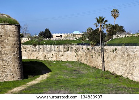 Morning time at the old town of Acco (Acre), Israel. Amongst the green weeds carpet, a path created by thousands of strolls fades into the shadow cast by the immense wall that rises above.