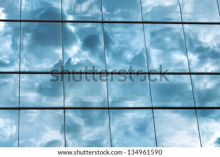 Cloudy sky reflecting off an office building\'s curtain wall made of square windows.