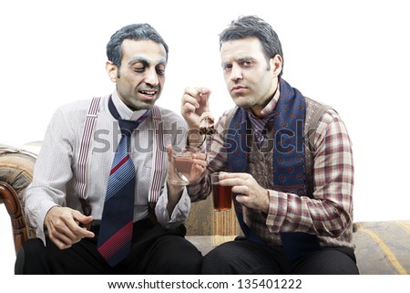 Two adult man (mid 30\'s and mid 20\'s) wearing old-man clothes and makeup, sitting on a used up vintage sofa. They\'re sharing a teabag. Isolated on white background.