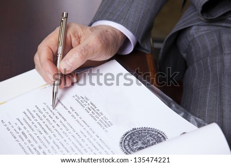 Close up on hands of a senior (in his 80\'s) businessman holding a fancy pen in his right hand, about to sign a contract. Seen from a high angle.