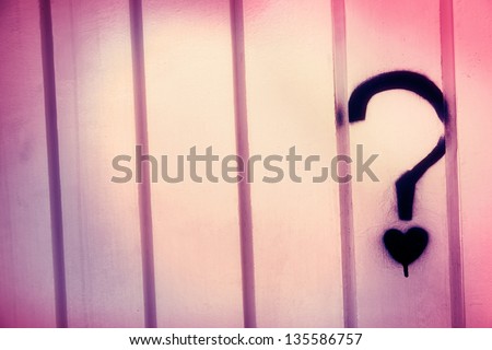 A blue graffiti in the shape of a question mark with a small heart instead of the dot, on a white metal wall with creases pattern.