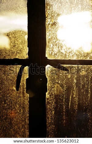 Afternoon yellow sun is back-lighting a window stained with drop marks, accentuating the texture and shapes.