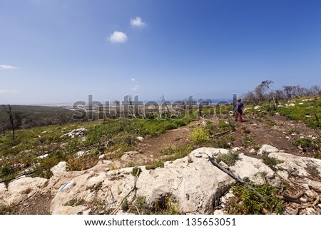 Wide angle long shot view of a senior woman in a field trip at the Carmel mountains in Israel. The Mediterranean sea and coastline (Atlit) can be seen in the background.