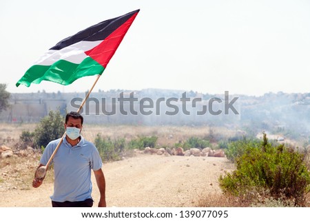 BIL\'IN, PALESTINE - MAY 17: A Palestinian protester holding the Palestine flag walking away from the wall of separation at a protest against the Israeli occupation on May 17, 2013 in Bil\'in, Palestine